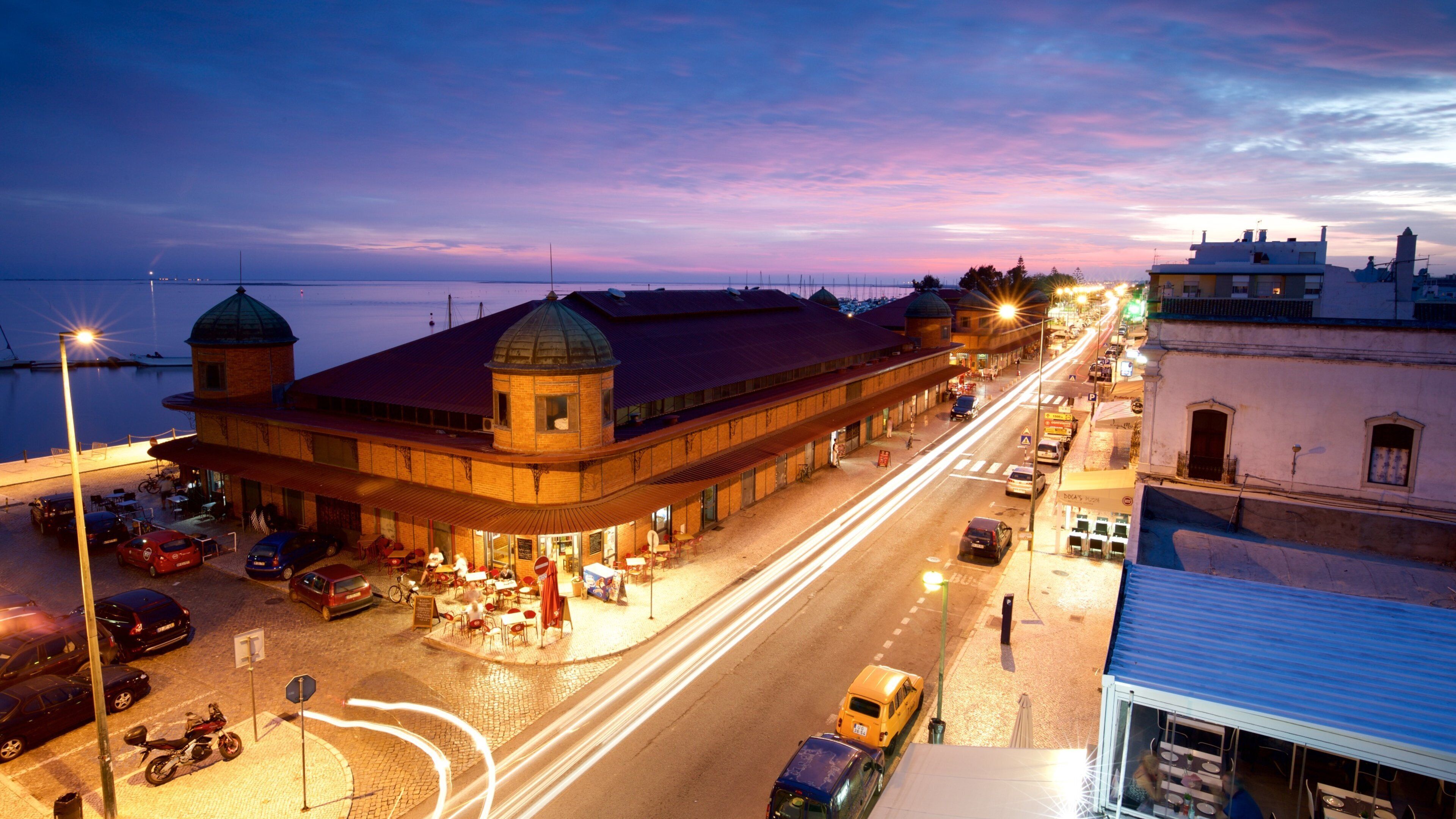 A waterfront street at dusk with a prominent building with a dome and a red roof.