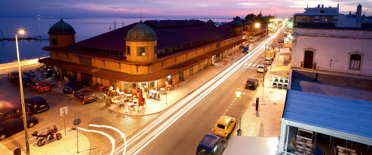 A waterfront street at dusk with a prominent building with a dome and a red roof.