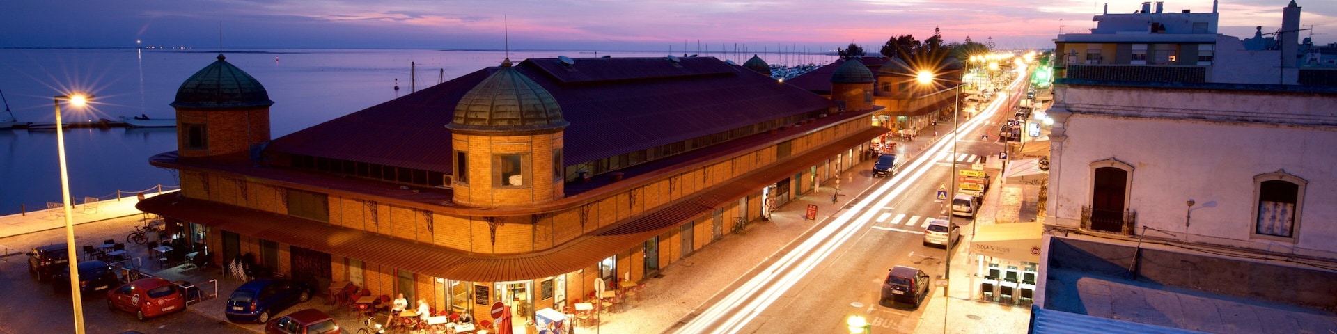 A waterfront street at dusk with a prominent building with a dome and a red roof.