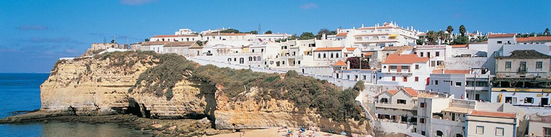 A coastal town with a sandy beach, clear blue sea, and white buildings on a cliff.
