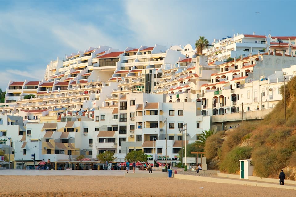 A coastal town with multi-story buildings, a sandy beach, and a rocky hillside.