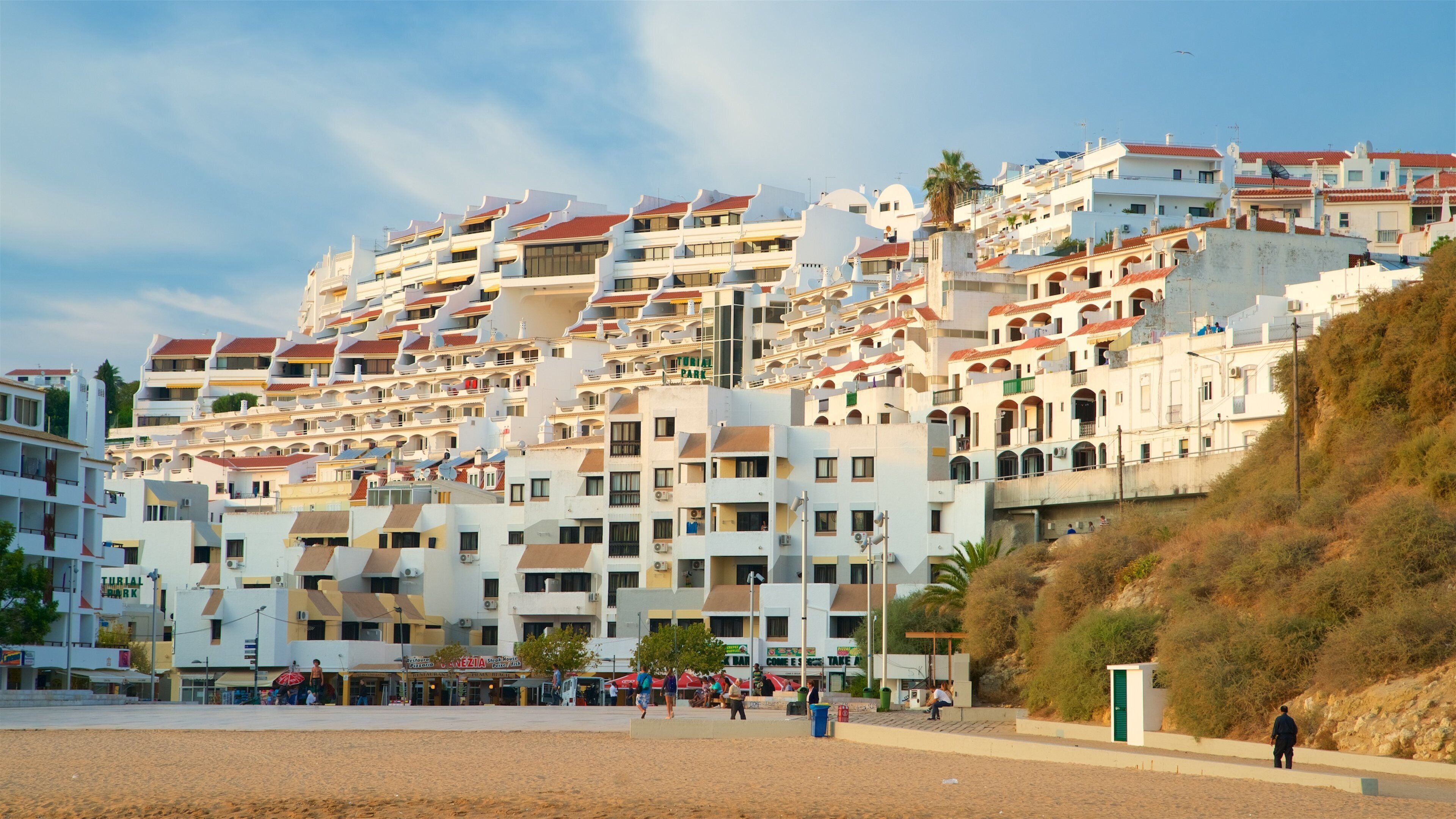 A coastal town with multi-story buildings, a sandy beach, and a rocky hillside.