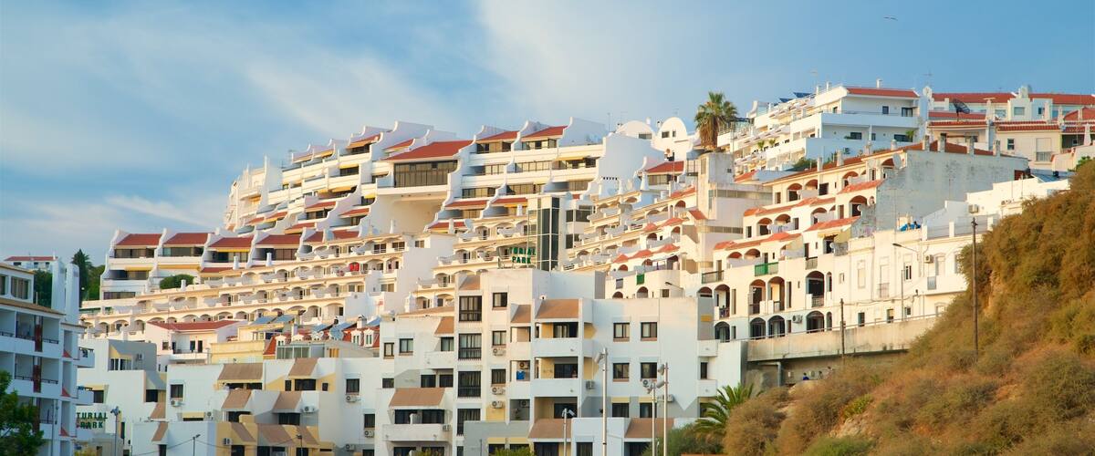 A coastal town with multi-story buildings, a sandy beach, and a rocky hillside.