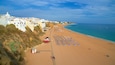 A beach with rows of sun loungers, a sandy shore, and buildings along the coastline.