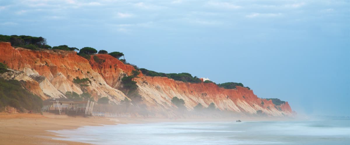 A beach with red cliffs and calm waves.