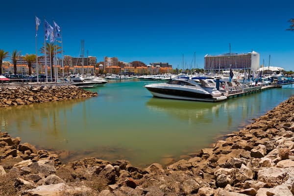 Un port de plaisance avec des bateaux amarrés, une côte rocheuse et un hôtel en arrière-plan.