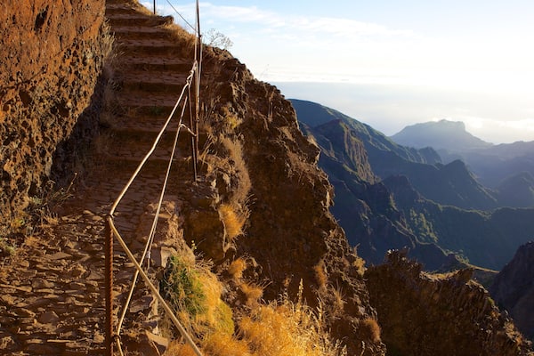 Un escalier en pierre, taillé à même la montagne, avec une vue sur les montagnes lointaines et un ciel dégagé.