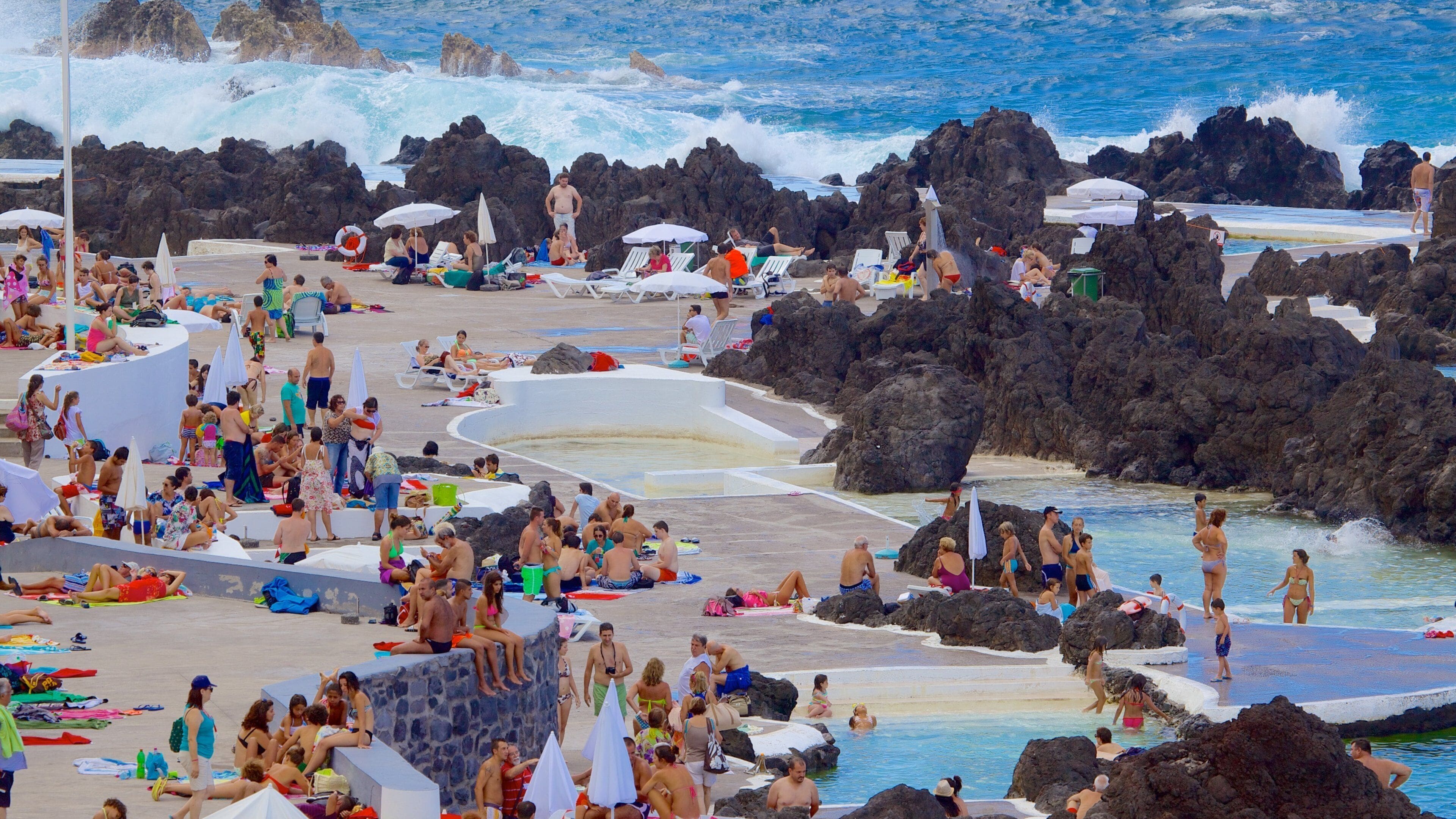 Uma praia movimentada com formações rochosas e uma área de piscina.