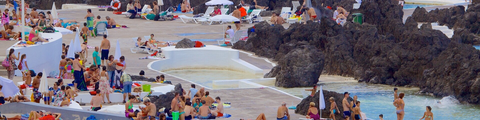 Uma praia movimentada com formações rochosas e uma área de piscina.