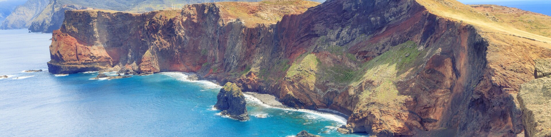 Un paisaje costero con acantilados, una formación rocosa destacada y un mar azul cristalino.