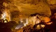 A cave with stalactites and stalagmites illuminated by artificial lighting.