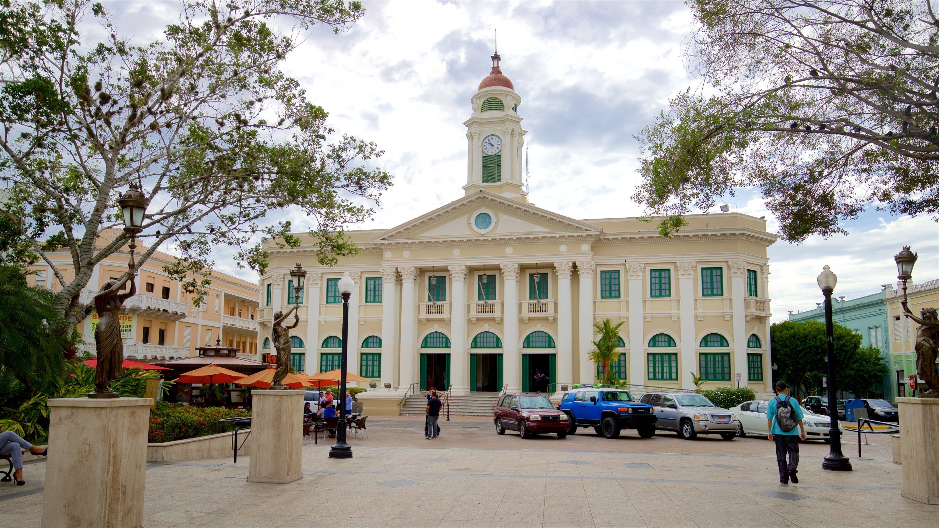 A historic building with a clock tower, surrounded by trees and outdoor seating areas.