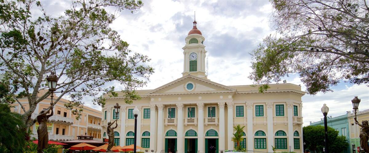 A historic building with a clock tower, surrounded by trees and outdoor seating areas.