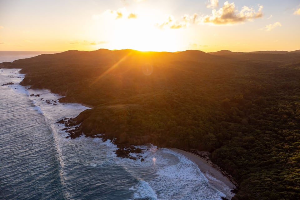 Paisaje costero con playa, olas y un atardecer.