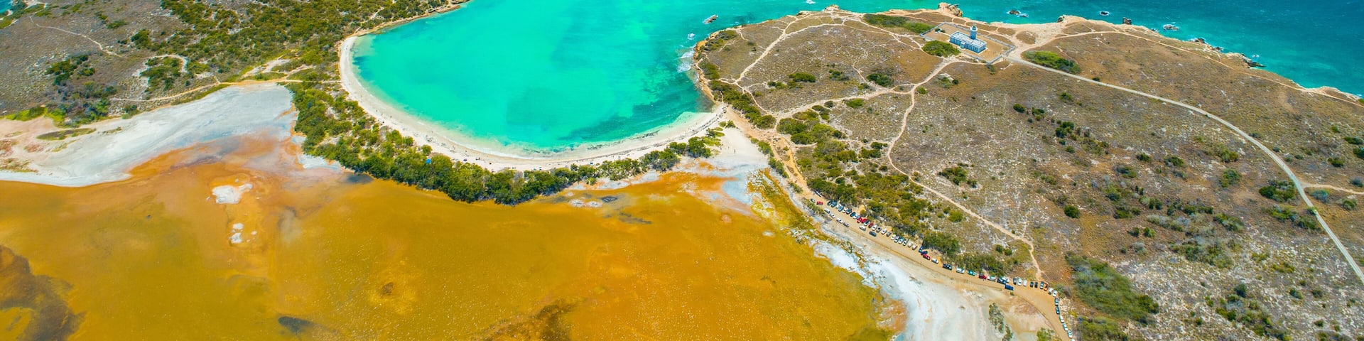 An aerial view of a coastal area with clear turquoise waters, a sandy beach, and a distinct yellowish water body.
