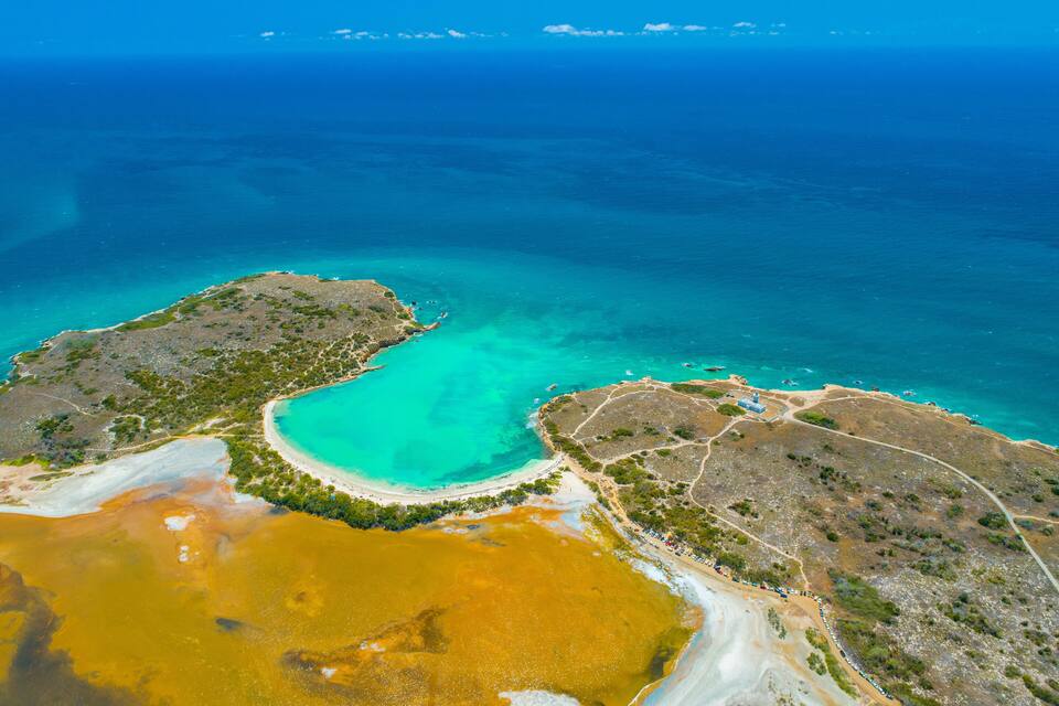 Vista aérea de una zona costera con aguas turquesas cristalinas, una playa arenosa y una masa de agua amarillenta bien definida.