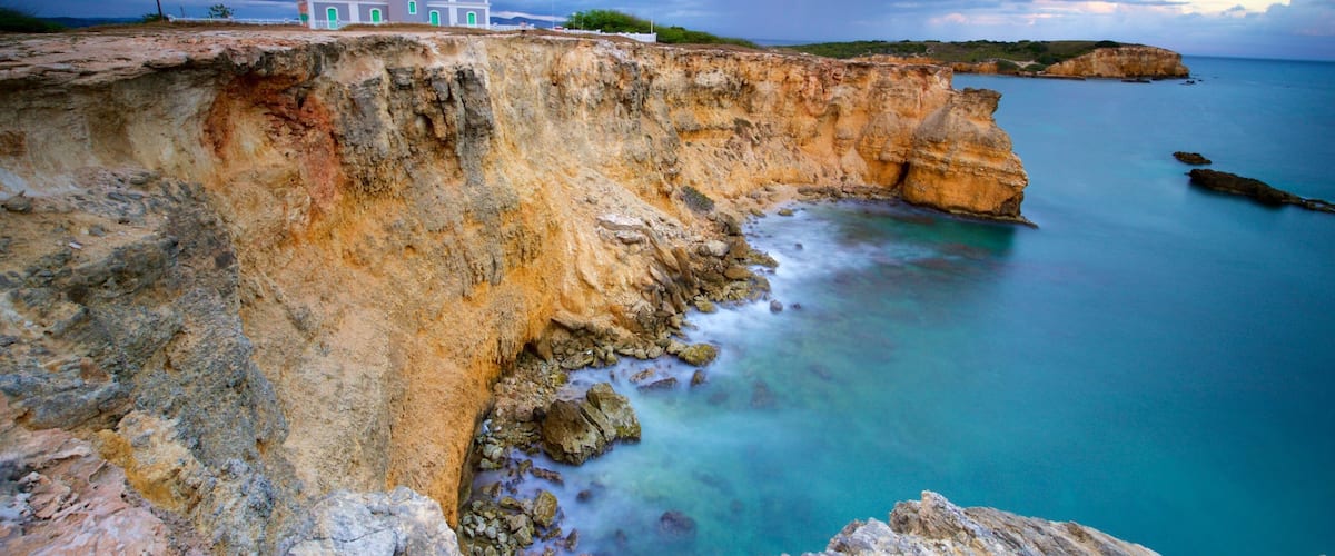 A coastal cliff with a lighthouse, clear blue sea, and rocky terrain.