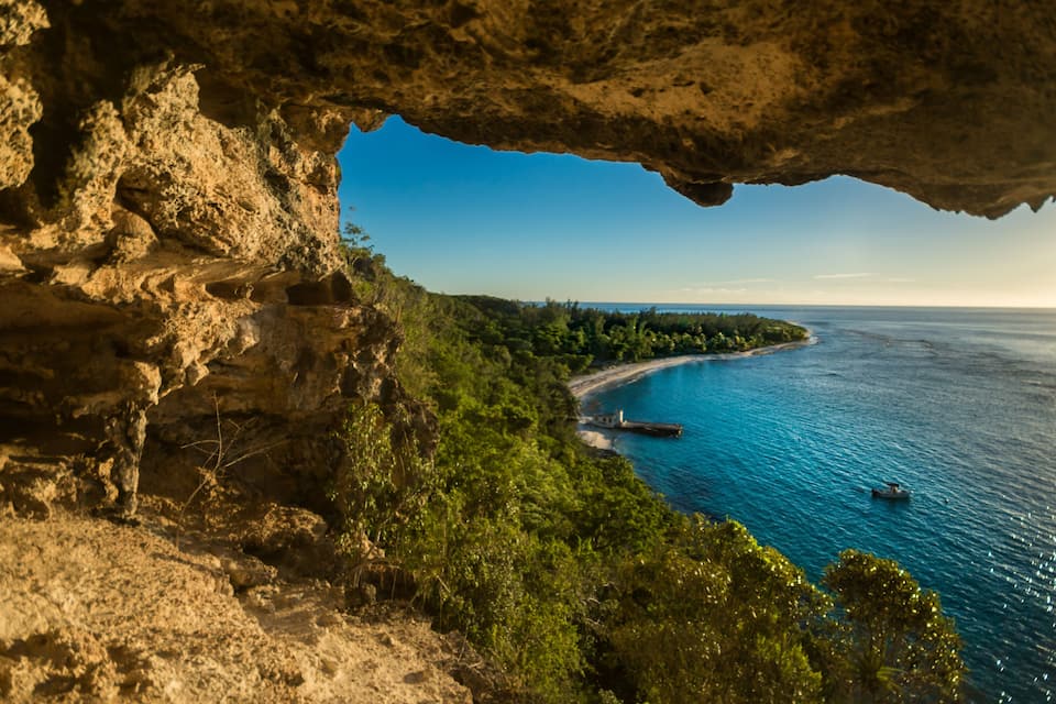 Paesaggio costiero con una scogliera rocciosa, mare cristallino e una piccola imbarcazione.