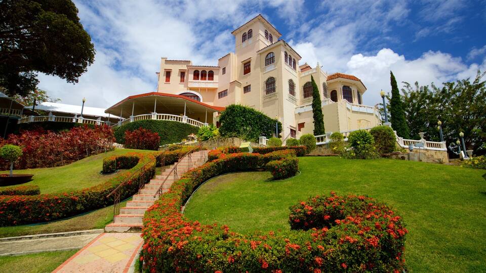 A large, historic building with a red-tiled roof, surrounded by well-manicured gardens and a sweeping staircase.