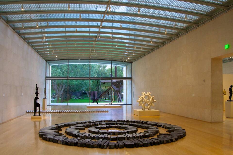 Een kunstgalerie met een grote, ronde sculptuur op de vloer, een sculptuur op een voetstuk, en een glazen plafond.