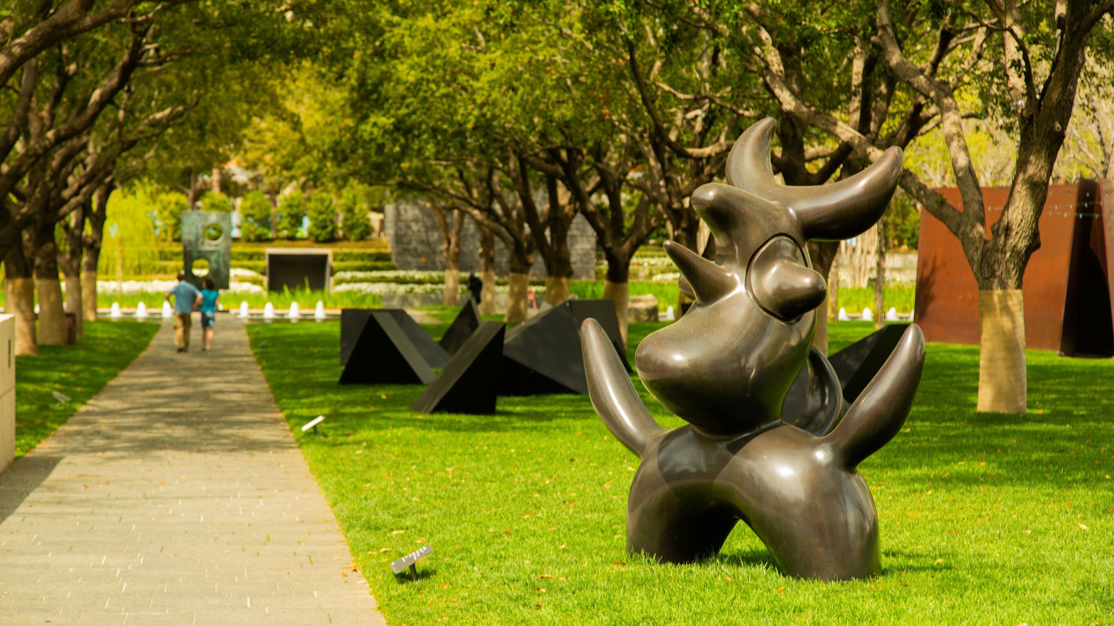 A sculpture of a stylized animal in a park with a pathway and trees.