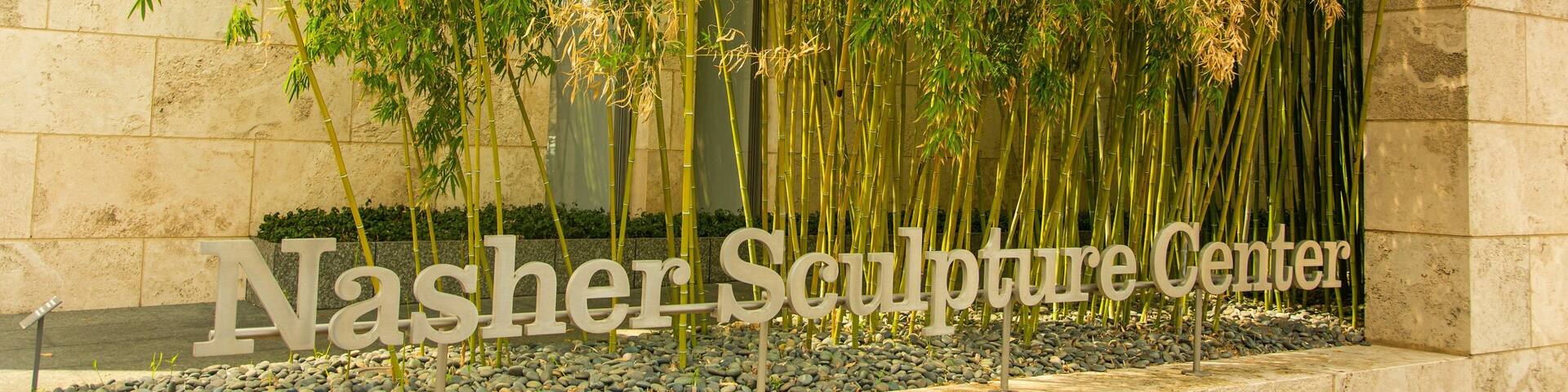 A sculpture garden with tall bamboo plants and a stone wall.
