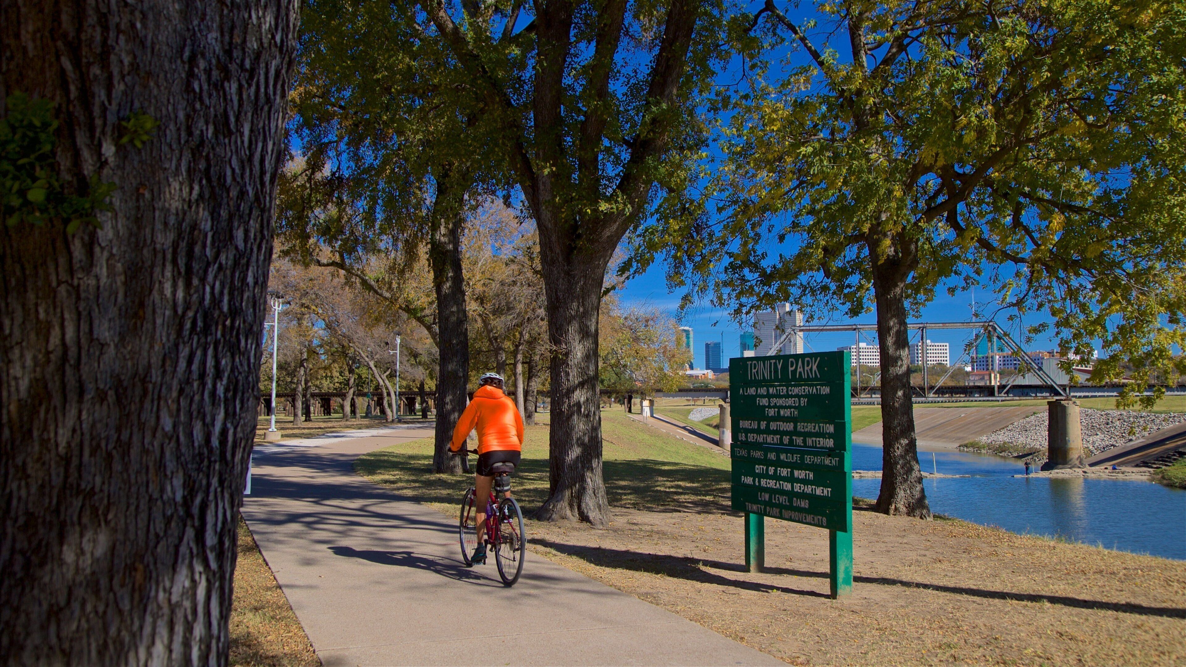 Ciclista en un camino pavimentado en el Parque Trinity, con un letrero que indica que es un área de conservación de tierra y agua.