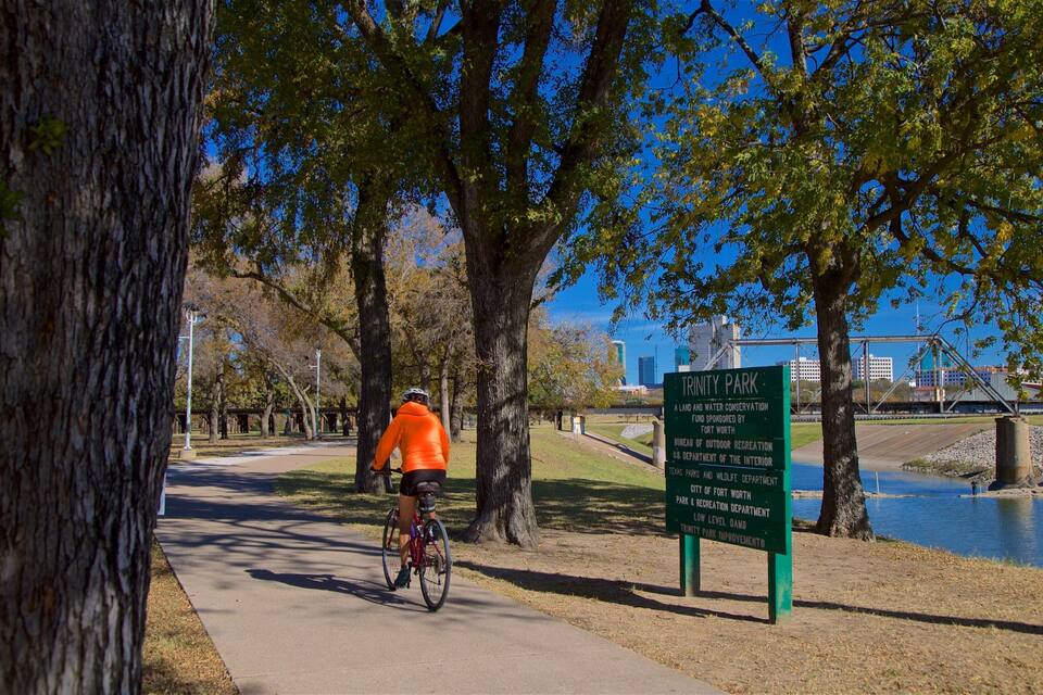 Ciclista en un camino pavimentado en el Parque Trinity, con un letrero que indica que es un área de conservación de tierra y agua.
