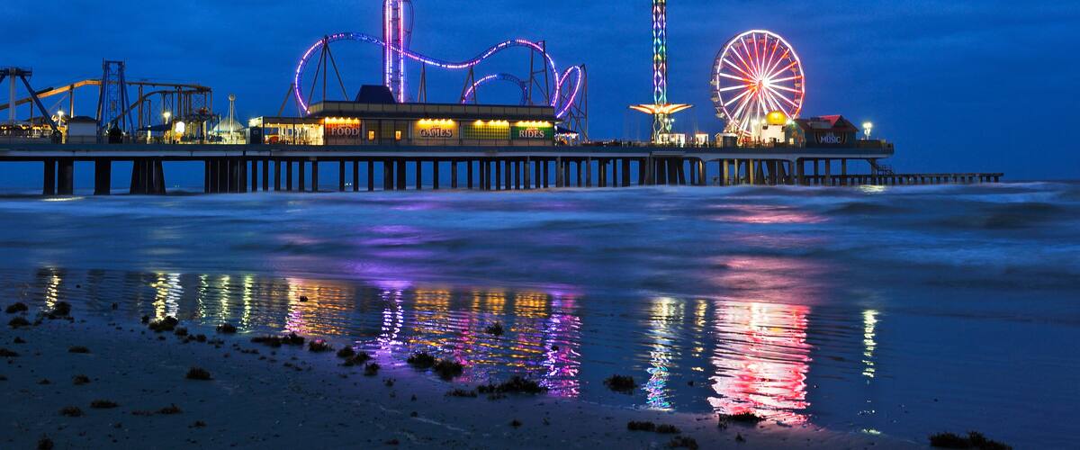 A pier with amusement rides and a Ferris wheel at night.