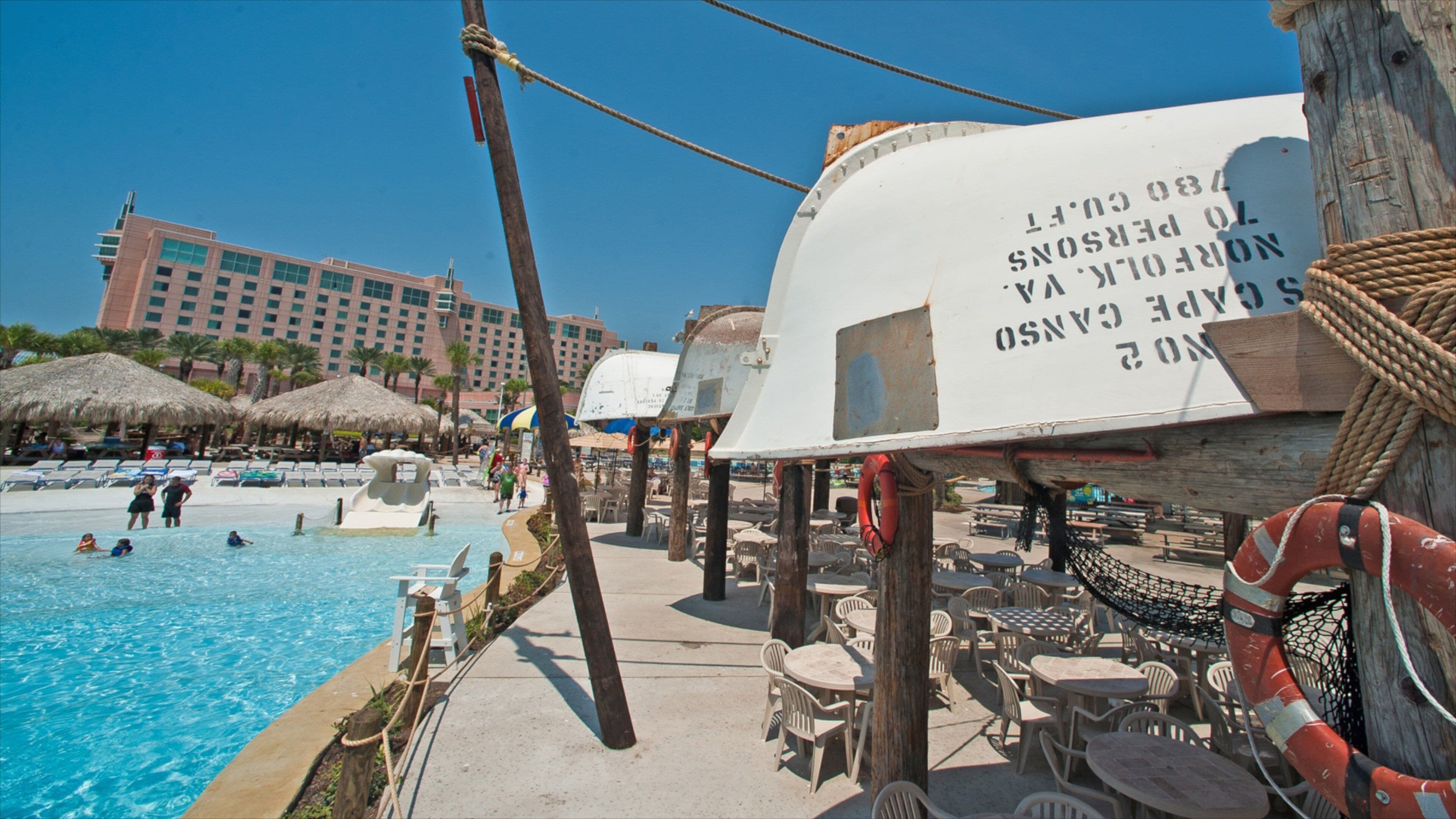 Una piscina con sillas de descanso y sombrillas, un flotador salvavidas y un cartel con texto.