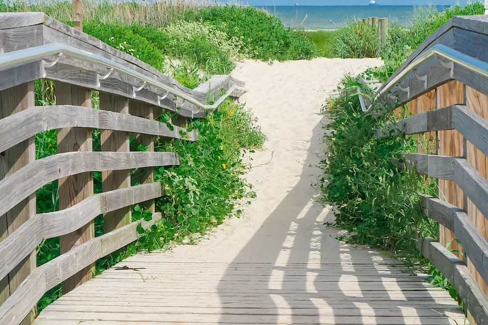 A wooden boardwalk leading to a sandy beach with green vegetation on either side.