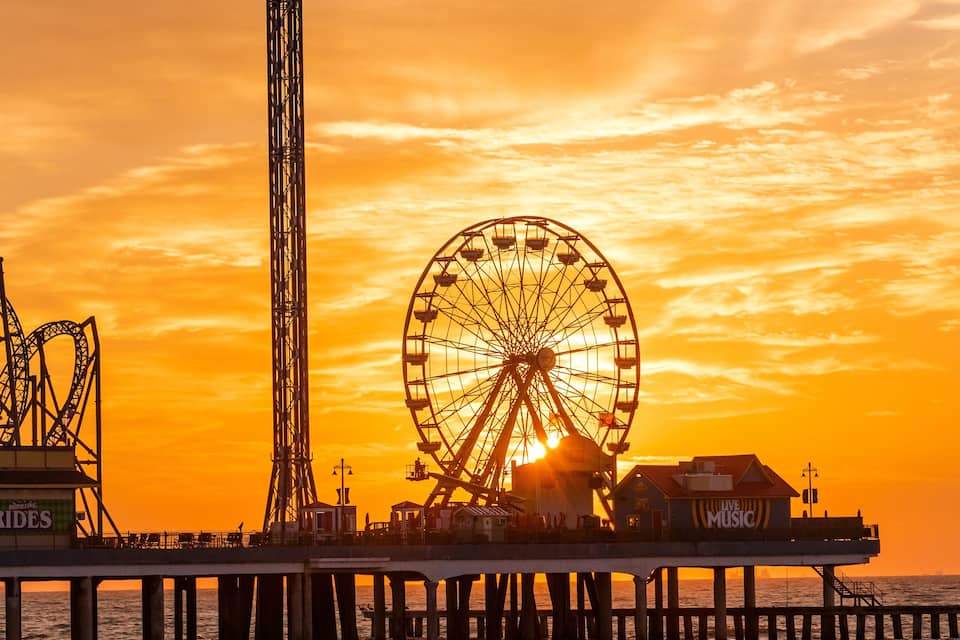 A pier with a Ferris wheel and a lighthouse at sunset.