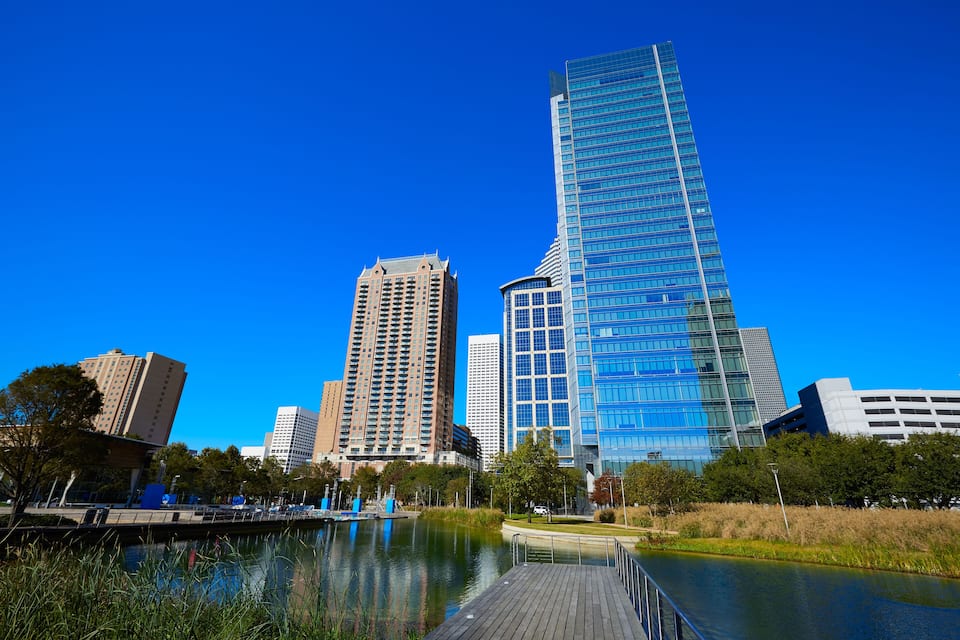 A cityscape with a river, a wooden dock, and modern high-rise buildings.