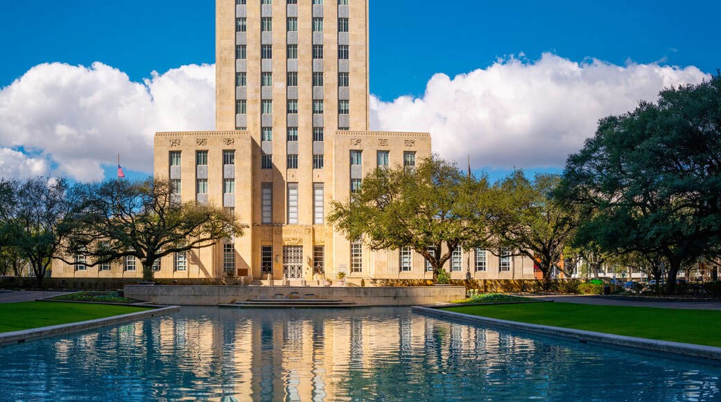 Houston City Hall building skyline, waving American Flags, and live oak trees with water reflections on the Herman Square water fountain in Texas, USA