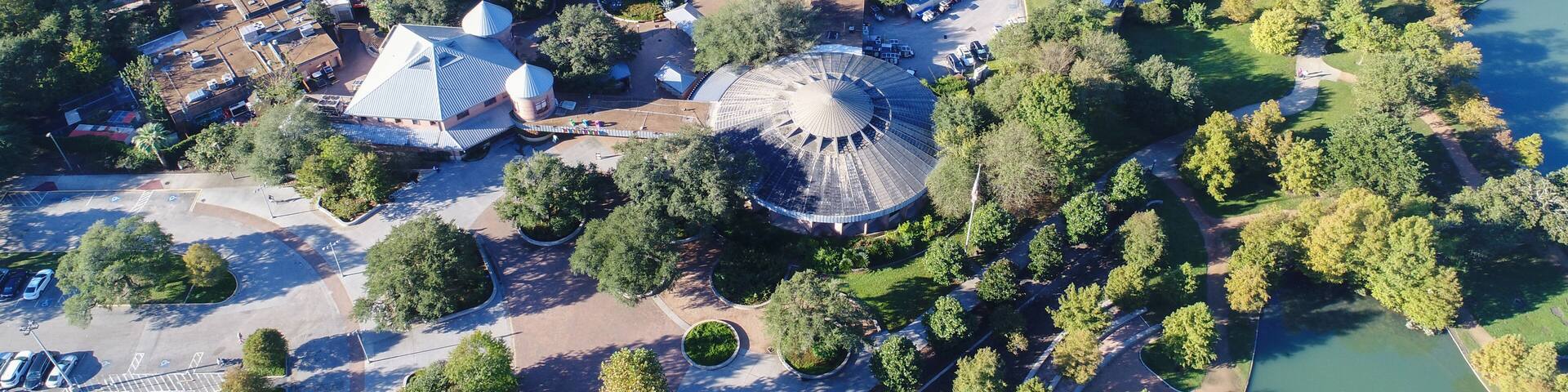 An aerial view of a park with a large dome structure, surrounded by trees and a body of water.