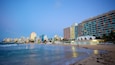 A beach with ocean waves, a city skyline, and a hotel with a distinctive white and orange facade.
