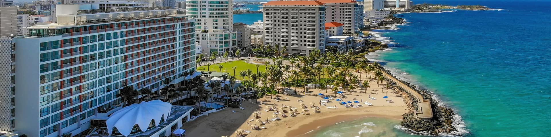 A coastal cityscape with a beachfront, high-rise hotels, and a clear blue sky.