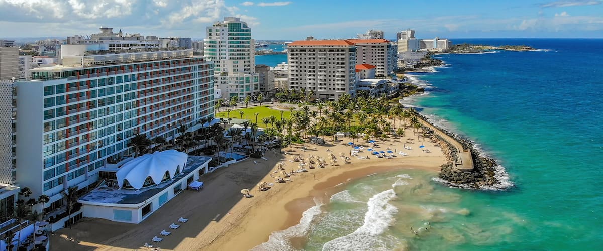 A coastal cityscape with a beachfront, high-rise hotels, and a clear blue sky.