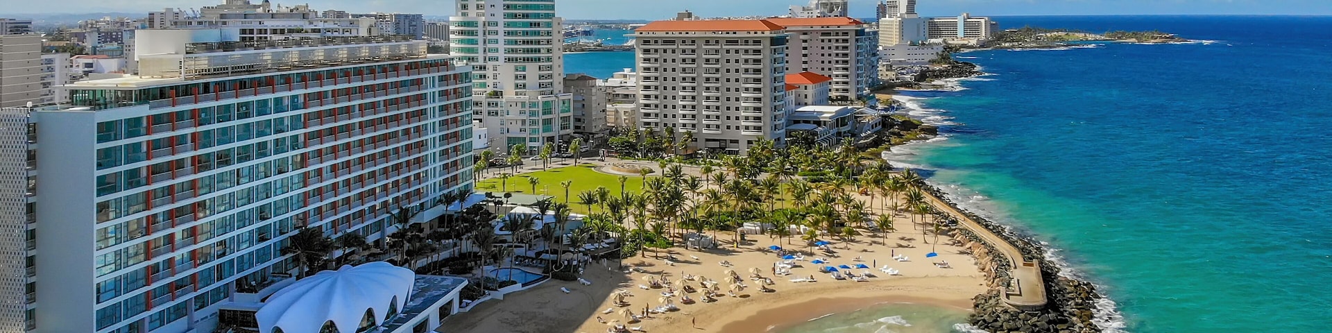 A coastal cityscape with a beachfront, high-rise hotels, and a clear blue sky.