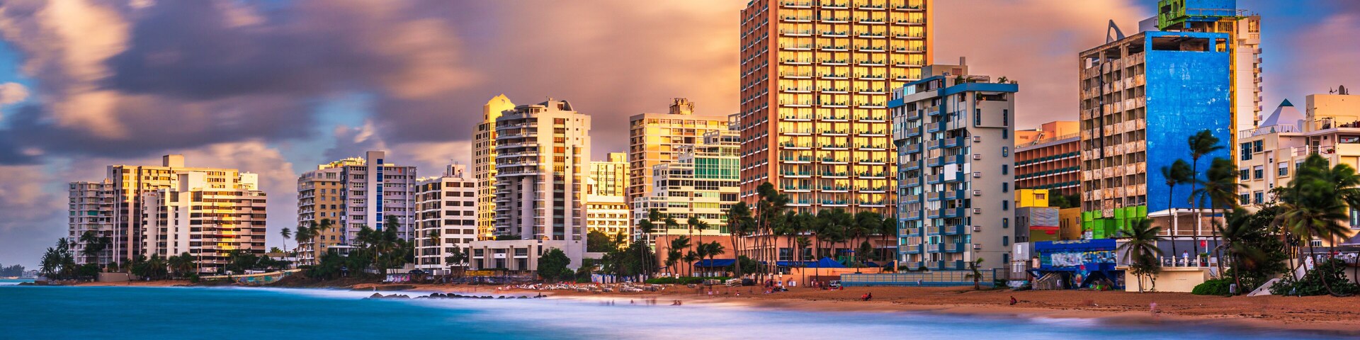 Un paisaje urbano costero con edificios altos, una playa y palmeras.