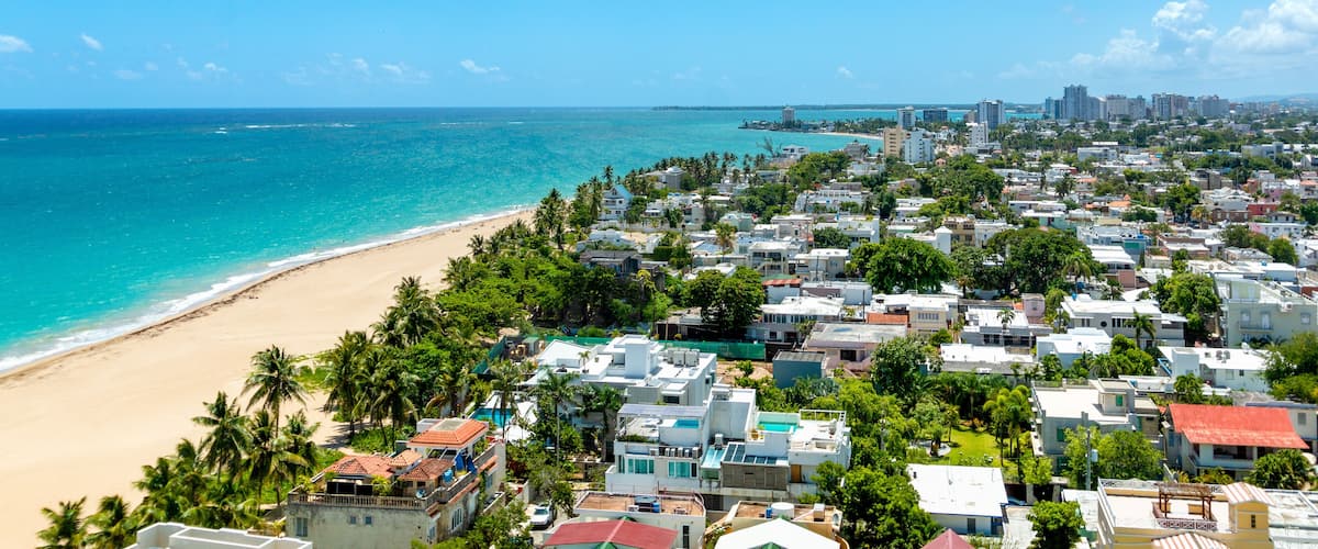 A coastal residential area with a beach, houses, and a distant city skyline.