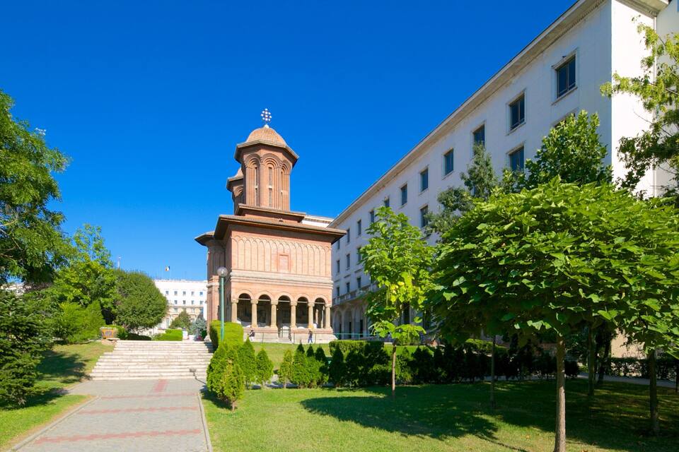 A historic building with a tower, surrounded by trees and a clear blue sky.