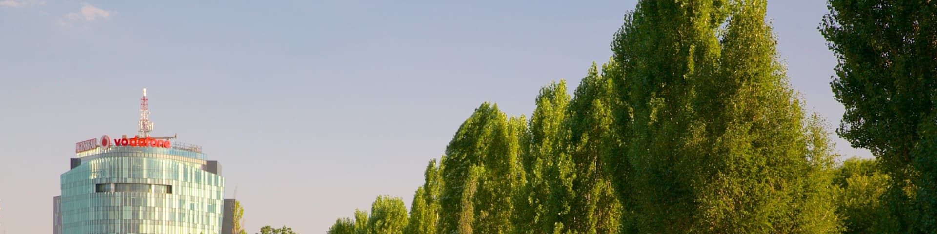 Un parque con vegetación exuberante, un edificio alto con la señalización 'Vodafone' y un cielo despejado.