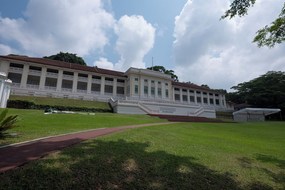 A large white colonial-style building with a red roof, surrounded by well-maintained lawns and a paved walkway.