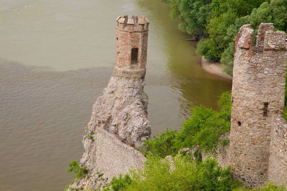 Two medieval stone towers by a river, surrounded by lush greenery.