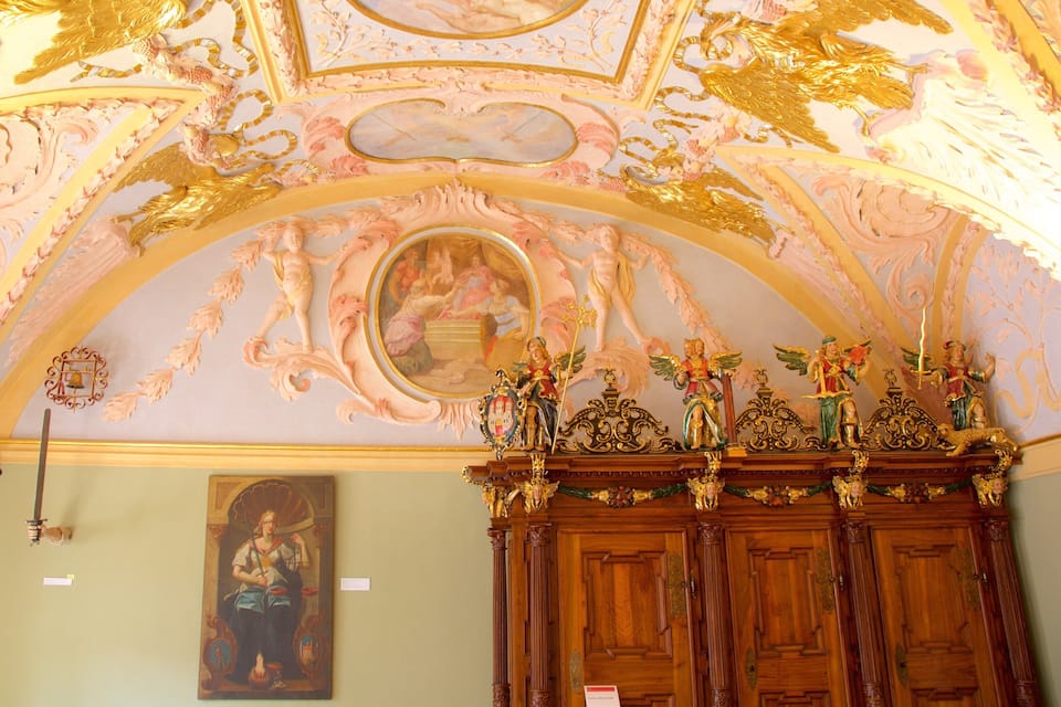 Un techo ornamentado con detalles dorados y un cuadro clásico.