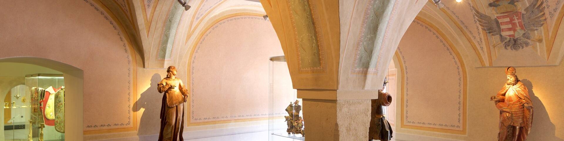 A museum interior with classical statues and ornate ceiling decorations.