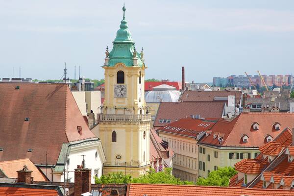A historic clock tower with a green dome, surrounded by traditional buildings with red-tiled roofs.