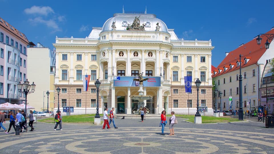 Un edificio histórico con arquitectura ornamentada, una fuente central y banderas.