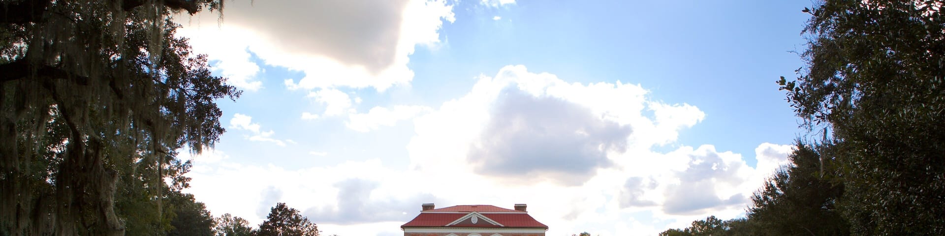 A large brick building with a red roof, surrounded by a grassy field and trees.